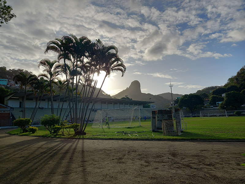 Vista do campo de futebol do campus, com palmeiras na frente e a Pedra dos Olhos ao fundo.