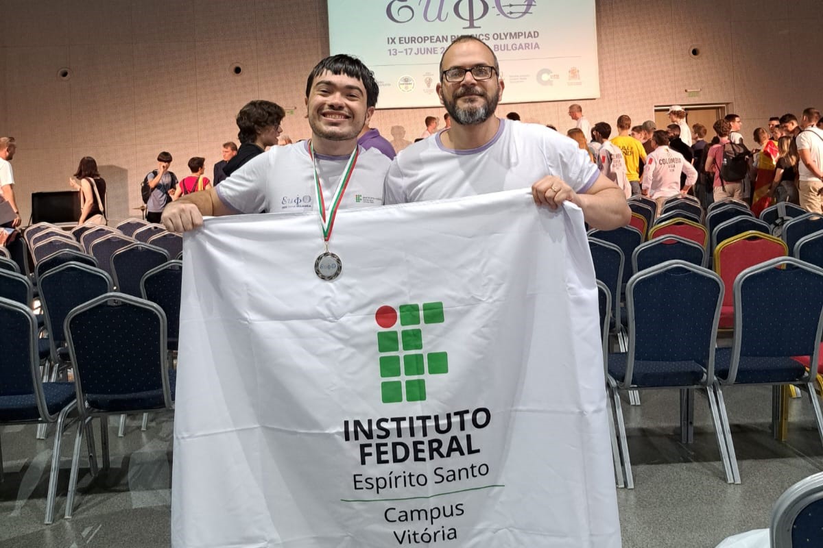 O estudante medalhista Patrick Avelar Santos Silva e o professor Judismar Guaitolini posam com a bandeira do Ifes na EuPhO.